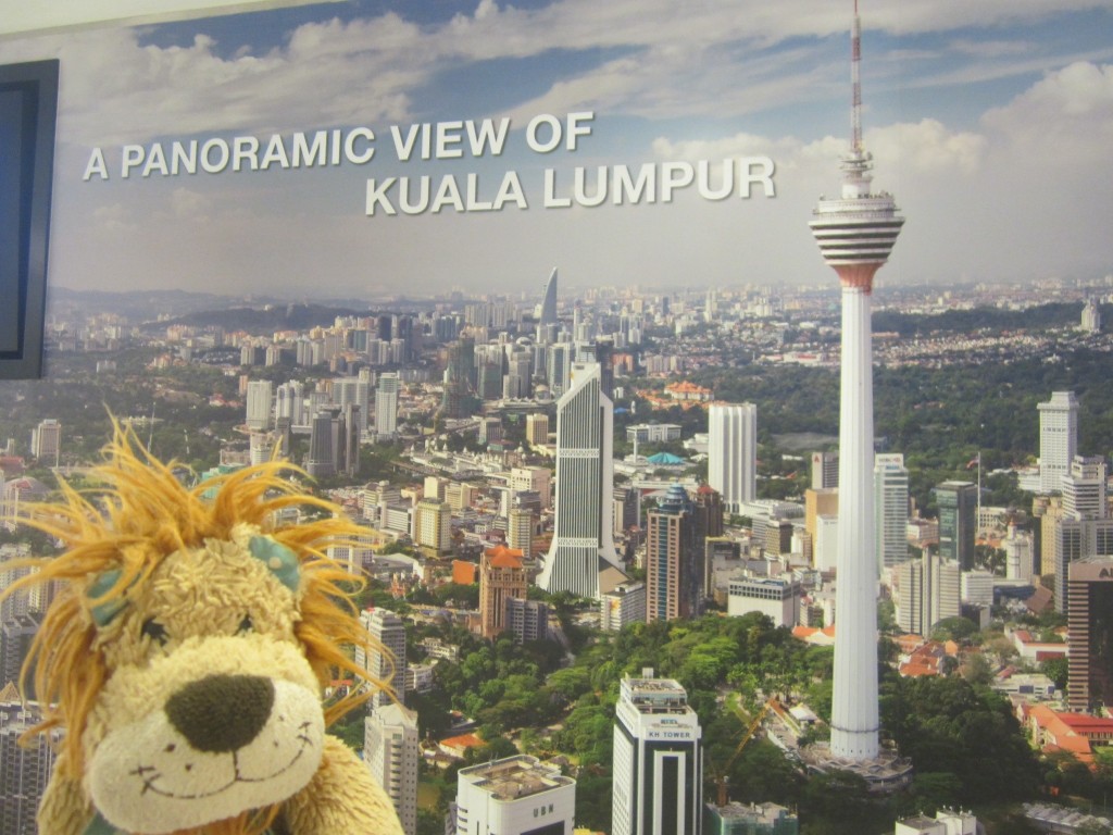 Lewis the Lion stands next to a poster of the KL skyline